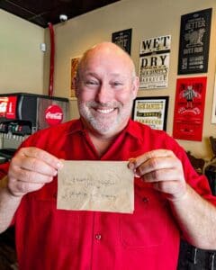 blane hunter, owner of porky butts bbq in omaha, ne, holds a napkin with a thank you written by a customer